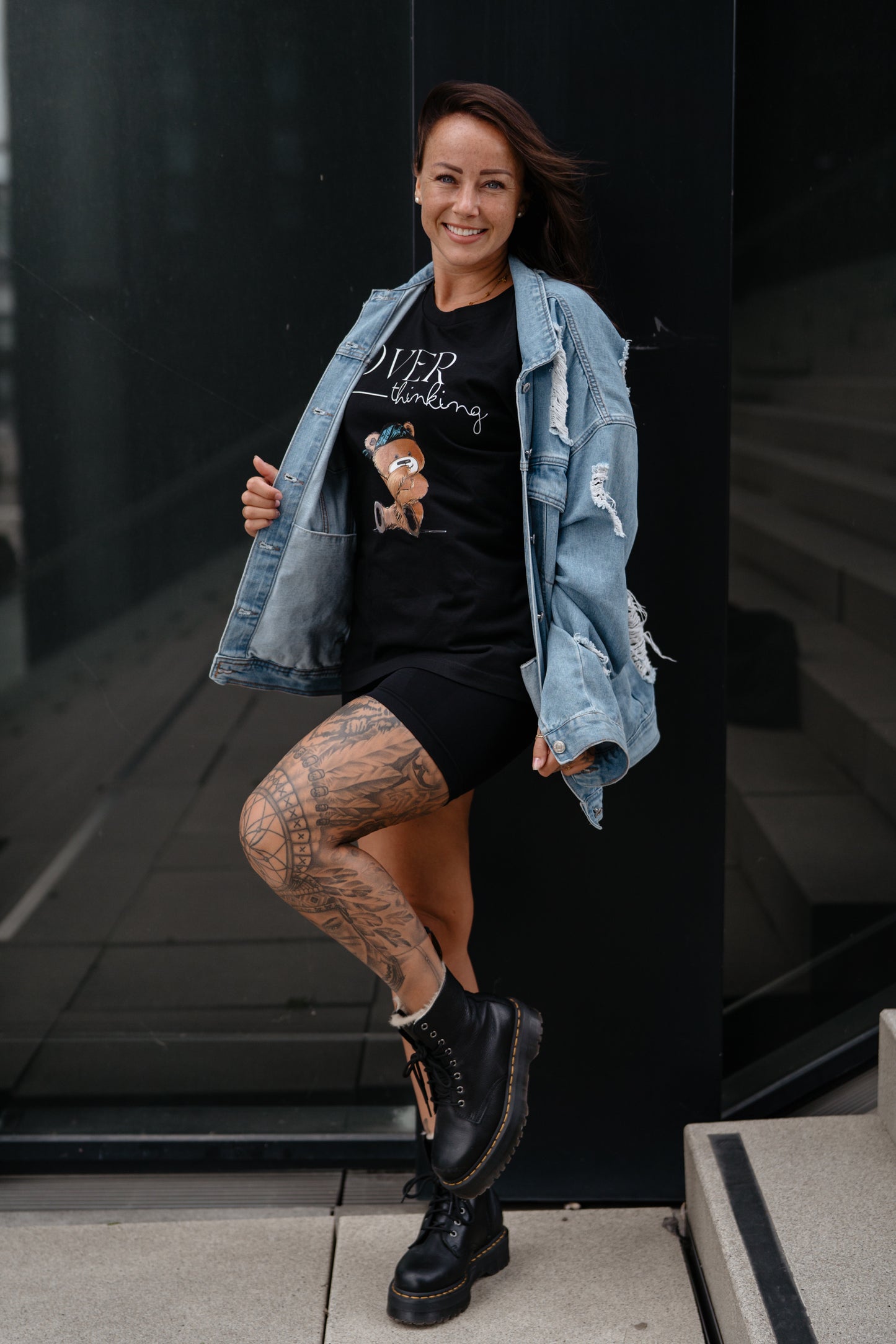 Schwarzes Unisex-T-Shirt mit großem Frontprint. Das Design zeigt den Schriftzug „OVER thinking“ in Weiß sowie eine Illustration eines nachdenklich wirkenden Teddybären mit blauer Bandana.