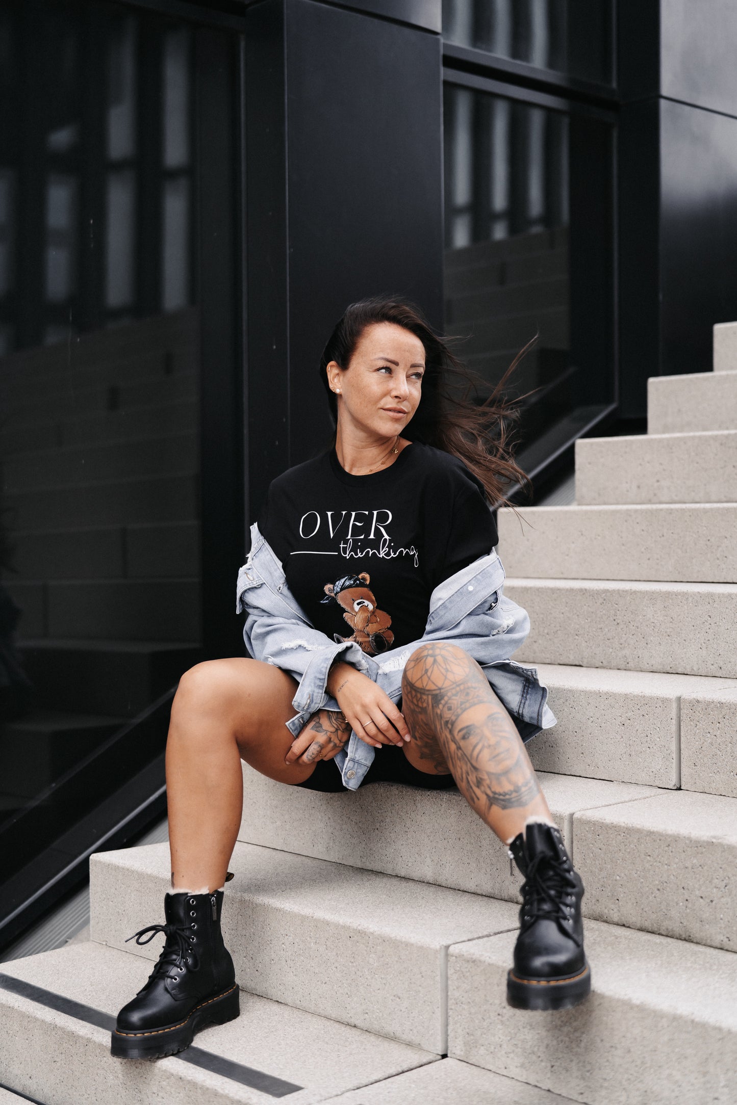 Schwarzes Unisex-T-Shirt mit großem Frontprint. Das Design zeigt den Schriftzug „OVER thinking“ in Weiß sowie eine Illustration eines nachdenklich wirkenden Teddybären mit blauer Bandana.
