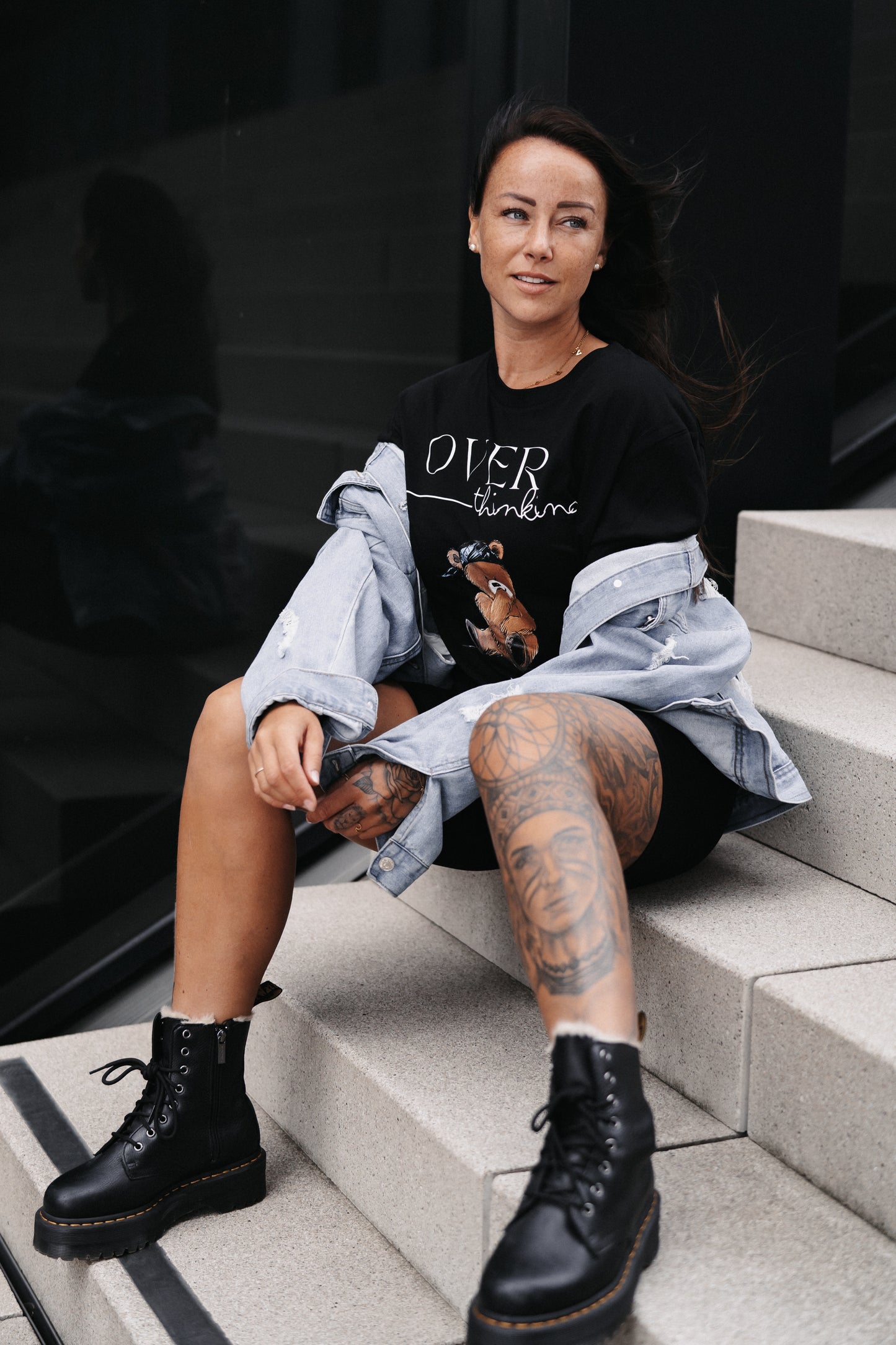 Schwarzes Unisex-T-Shirt mit großem Frontprint. Das Design zeigt den Schriftzug „OVER thinking“ in Weiß sowie eine Illustration eines nachdenklich wirkenden Teddybären mit blauer Bandana.