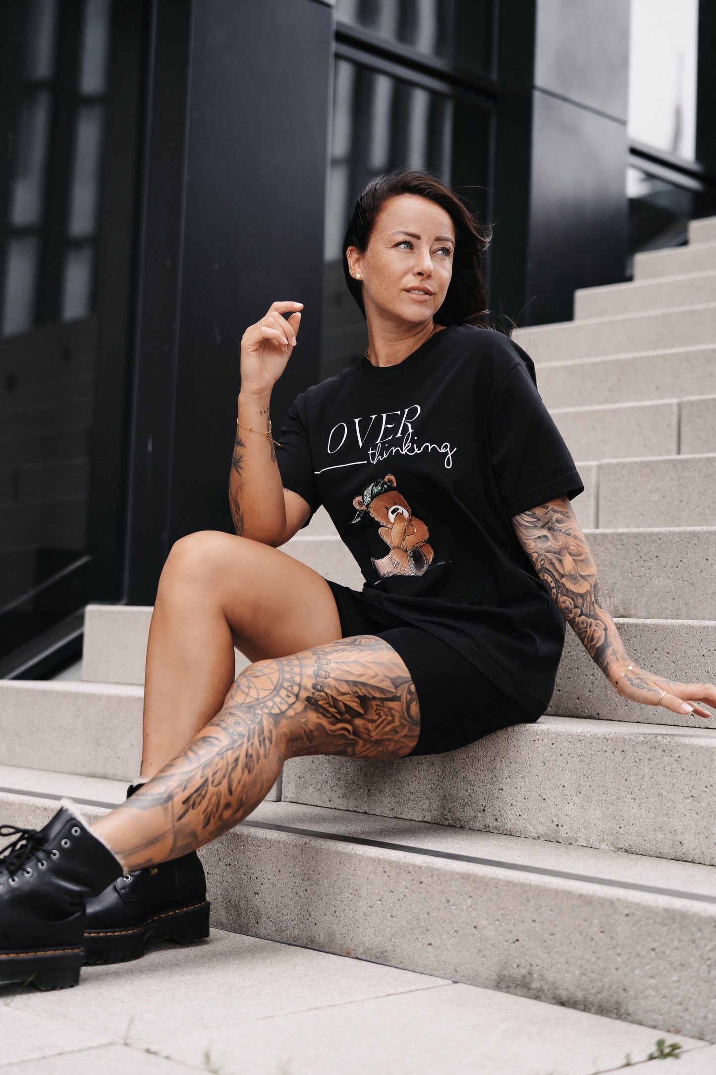 Schwarzes Unisex-T-Shirt mit großem Frontprint. Das Design zeigt den Schriftzug „OVER thinking“ in Weiß sowie eine Illustration eines nachdenklich wirkenden Teddybären mit grünem Bandana