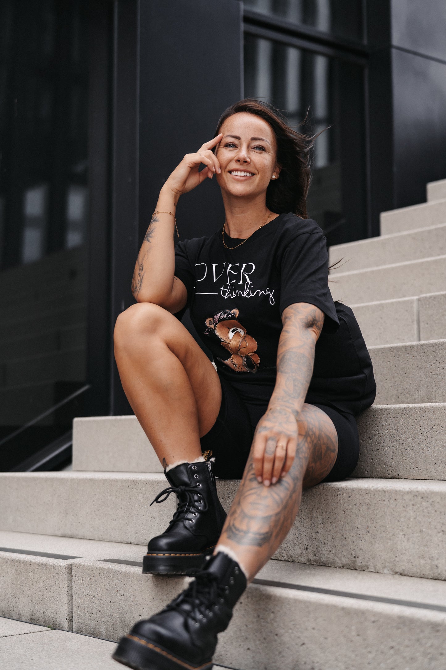 Schwarzes Unisex-T-Shirt mit großem Frontprint. Das Design zeigt den Schriftzug „OVER thinking“ in Weiß sowie eine Illustration eines nachdenklich wirkenden Teddybären mit pinkem Bandana.