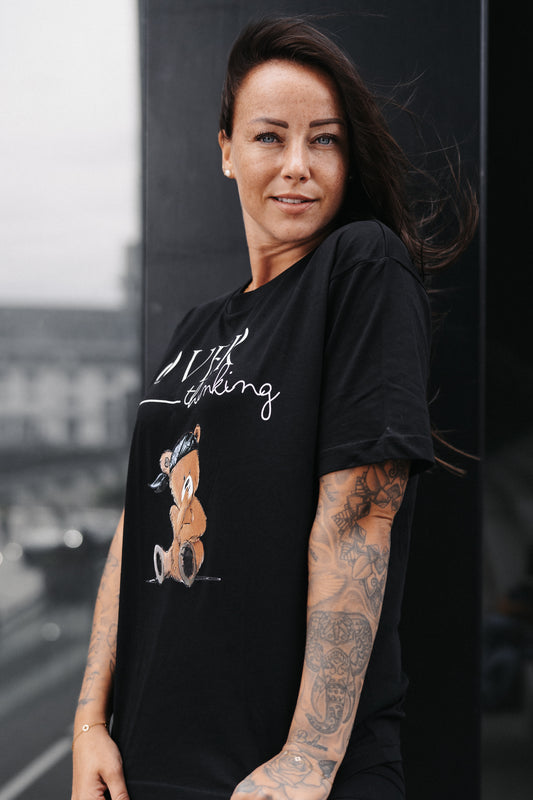 Schwarzes Unisex-T-Shirt mit großem Frontprint. Das Design zeigt den Schriftzug „OVER thinking“ in Weiß sowie eine Illustration eines nachdenklich wirkenden Teddybären mit grünem Bandana.