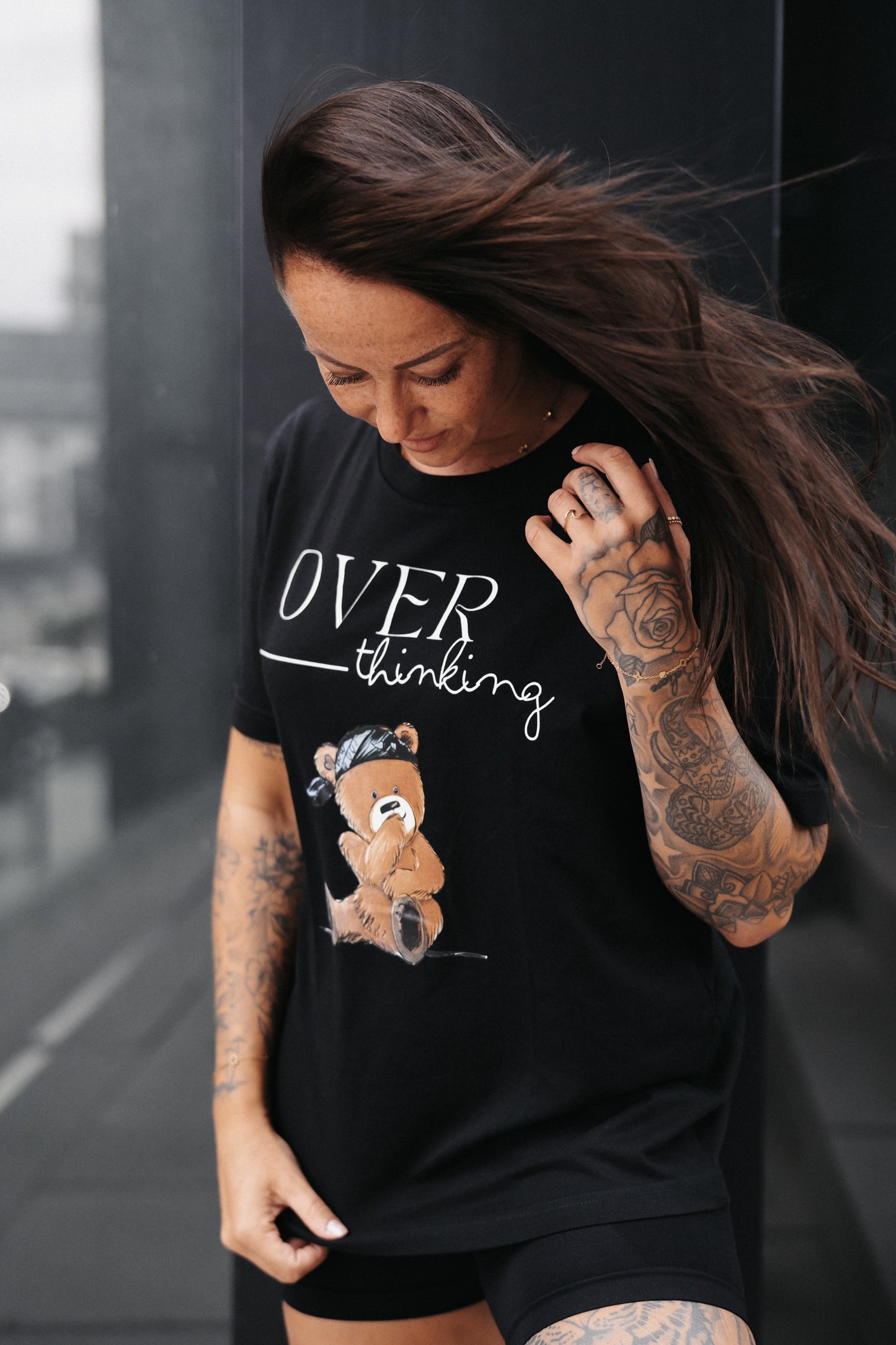 Schwarzes Unisex-T-Shirt mit großem Frontprint. Das Design zeigt den Schriftzug „OVER thinking“ in Weiß sowie eine Illustration eines nachdenklich wirkenden Teddybären mit grünem Bandana.
