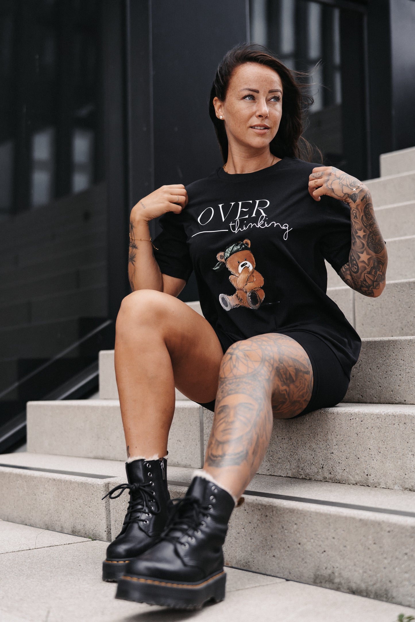 Schwarzes Unisex-T-Shirt mit großem Frontprint. Das Design zeigt den Schriftzug „OVER thinking“ in Weiß sowie eine Illustration eines nachdenklich wirkenden Teddybären mit grünem Bandana.