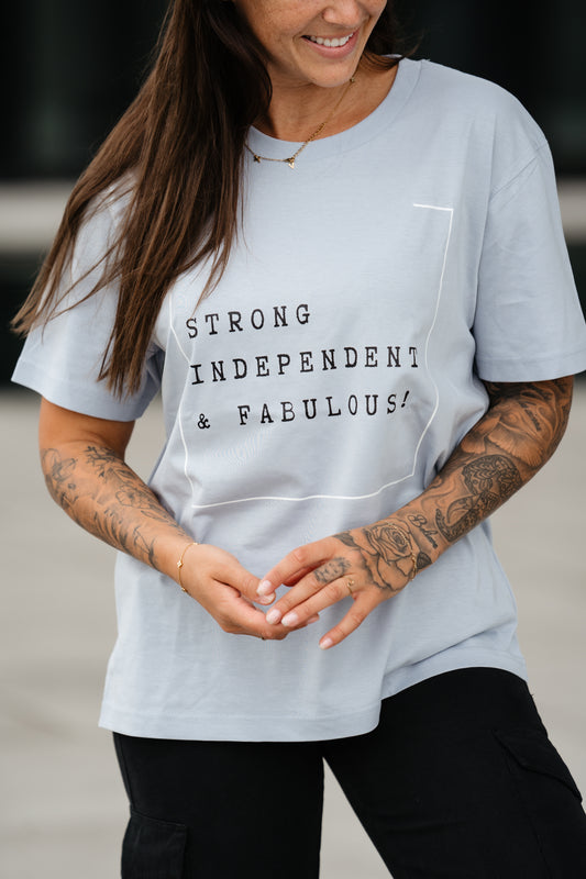 Hellblaues T-Shirt mit schwarzem Frontprint in Schreibmaschinenoptik. Der Aufdruck zeigt den Slogan: „STRONG INDEPENDENT & FABULOUS!“ innerhalb eines dezenten weißen Rahmens.