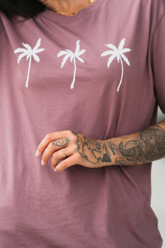 Lässiges T-Shirt in Altrosa mit weißem Palmen-Print auf der Vorderseite. Das Shirt hat einen lockeren Schnitt und besteht aus weichem Baumwollmaterial.