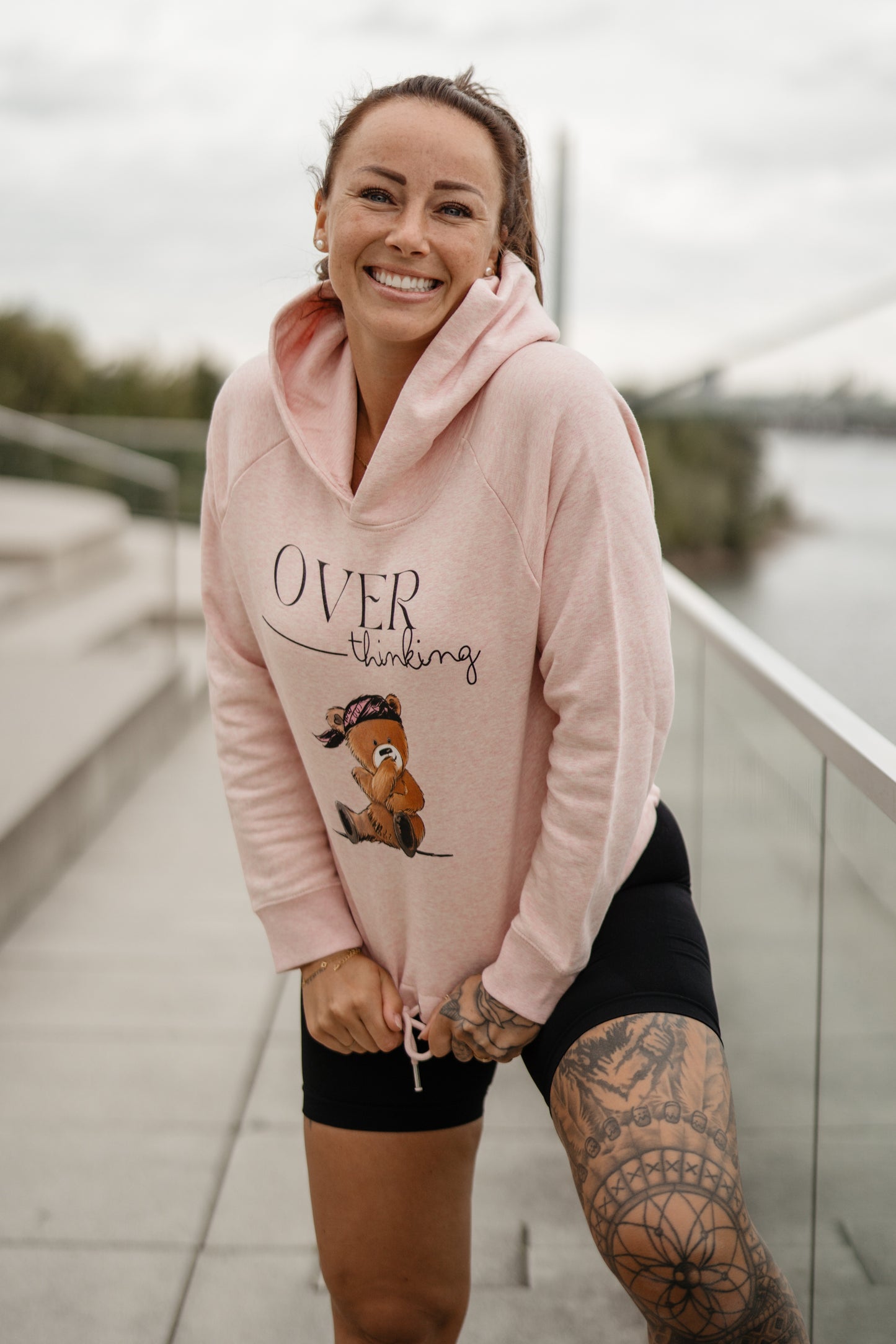 Hellrosa Damen-Hoodie mit Frontprint „OVERthinking“ und einem illustrierten Bärenmotiv. Der Kapuzenpullover hat eine Kordel am Bund zum Binden, lange Ärmel und eine weiche, leicht melierte Optik.