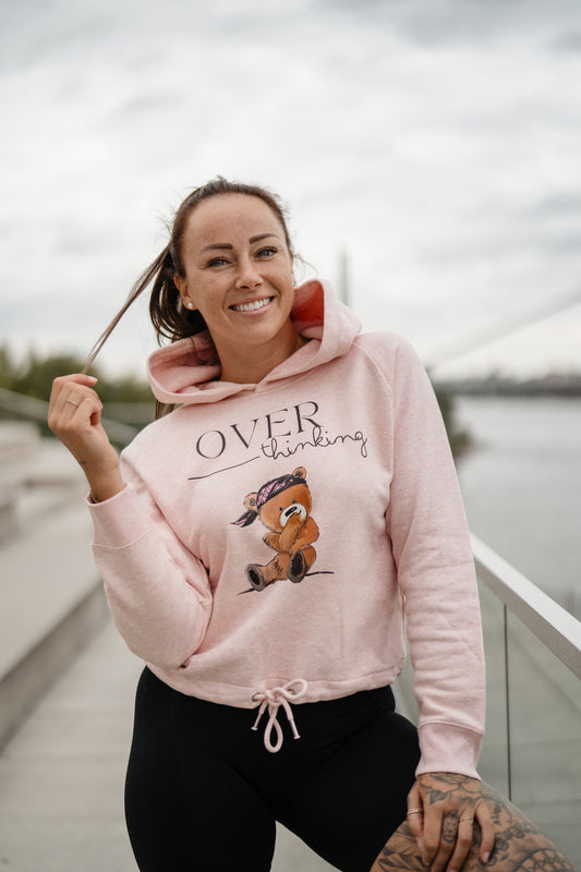 Hellrosa Damen-Hoodie mit Frontprint „OVERthinking“ und einem illustrierten Bärenmotiv. Der Kapuzenpullover hat eine Kordel am Bund zum Binden, lange Ärmel und eine weiche, leicht melierte Optik.