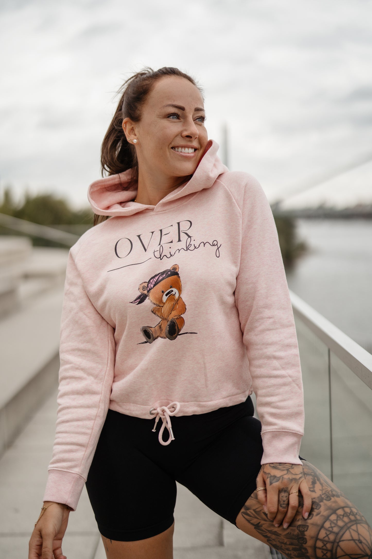 Hellrosa Damen-Hoodie mit Frontprint „OVERthinking“ und einem illustrierten Bärenmotiv. Der Kapuzenpullover hat eine Kordel am Bund zum Binden, lange Ärmel und eine weiche, leicht melierte Optik.