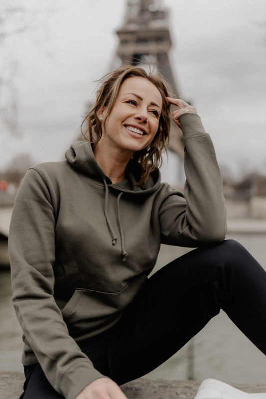 Person trägt einen dunkelgrünen Hoodie mit großem weißen Rückendruck eines nachdenklich sitzenden Teddybären mit Stirnband und dem Schriftzug „Overthinking…“. Das Sweatshirt wird im urbanen Außenbereich getragen, der Fokus liegt auf dem Design auf dem Rücken.